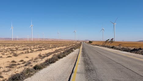 Generación-De-Energía-Limpia-Y-Sostenible-A-Partir-De-Un-Parque-De-Turbinas-Eólicas-Con-Un-Camino-Largo-Y-Recto-En-El-Paisaje-Del-Desierto-árabe-De-Jordania,-Oriente-Medio