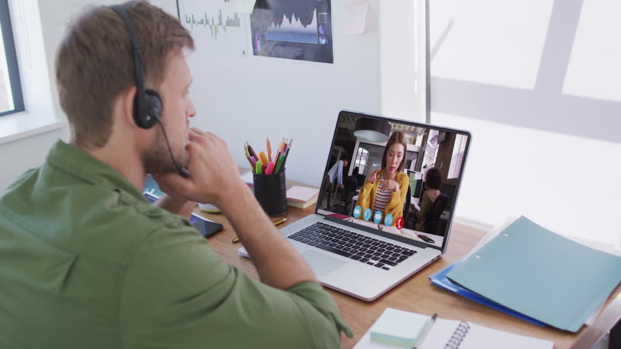 En kaukasisk mand med telefonheadset holder et videomøde med en kvindelig kollega på sin bærbare computer på kontoret.