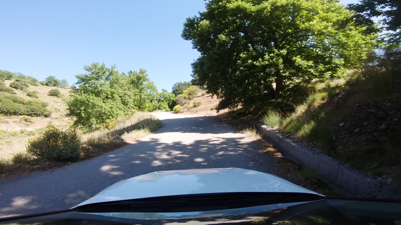 punto de vista del conductor de un camión blanco que gira a la derecha en una carretera de montaña con parabrisas reflectante y luz solar brillante que brilla a través de árboles verdes en el campo del sur de europa