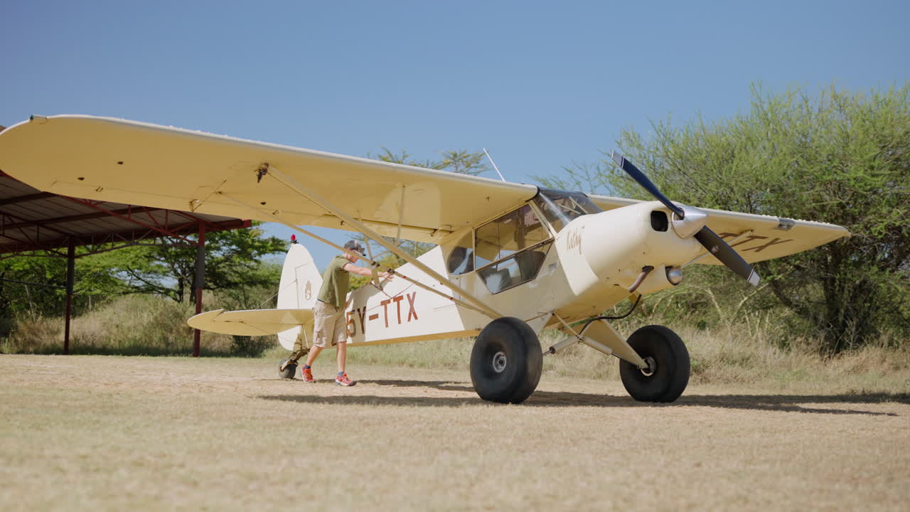 Mann inspiserer lite bushfly på gressflystripe i Afrika.