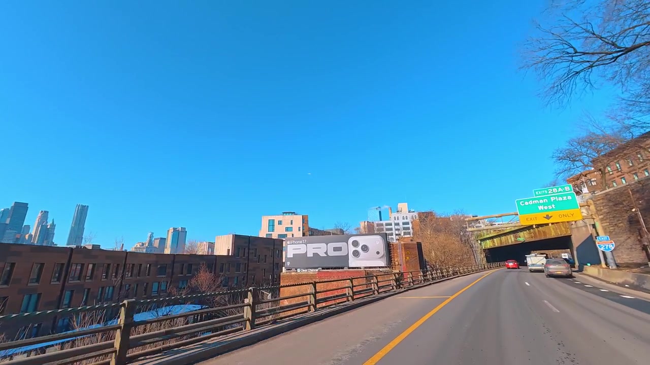 ニューヨークの高速道路の高架下から見たロウアーマンハッタンのスカイラインとイーストリバー。アスファルトの道路からの眺めは、青空の下、コンクリート構造物の下、水辺にそびえる高層ビル群を示している