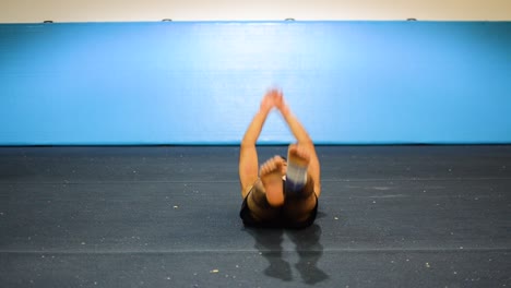 a-static-shot-of-a-guy-in-a-gymnastics-gym-doing-ab-workout-with-leg-raises-shirtless-from-a-side-front-view