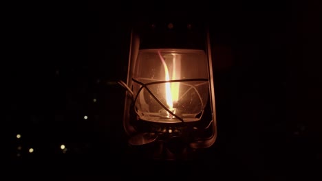 oil lantern with orange flame swings on its handle on black background