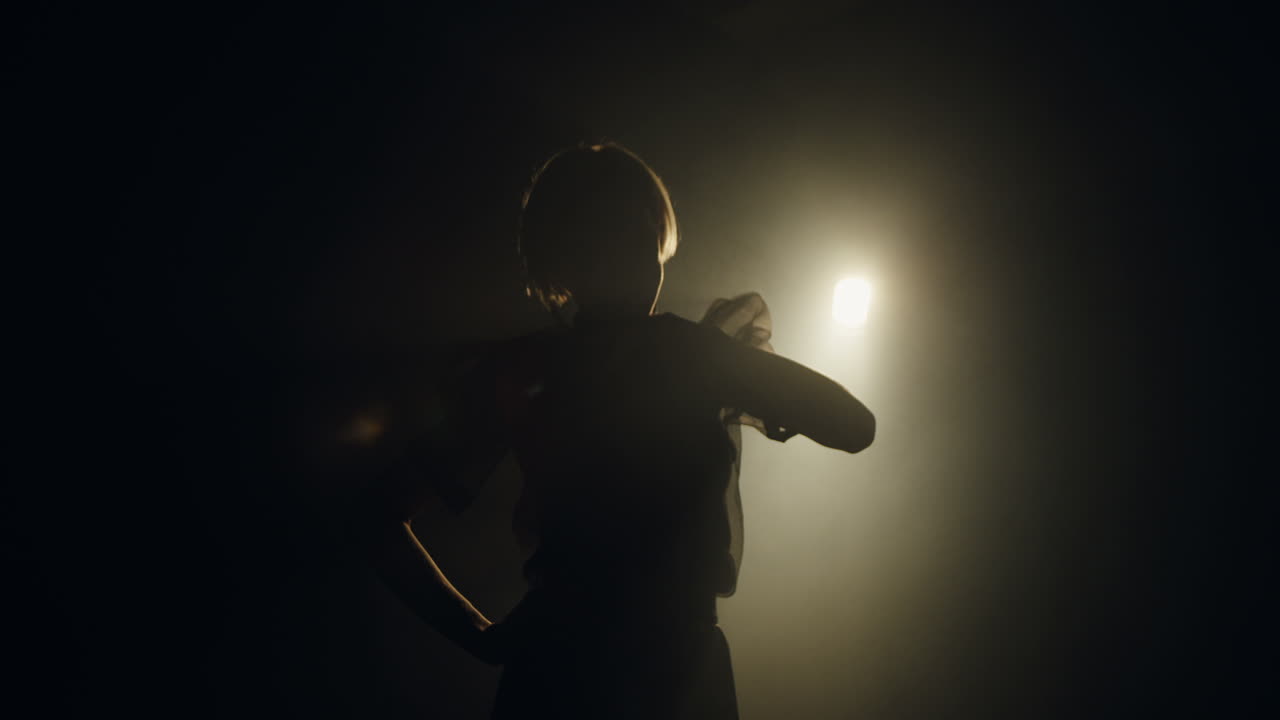 Beauty art photosession in a dark studio with a single spotlight source lighting on the female model silhouette changing poses