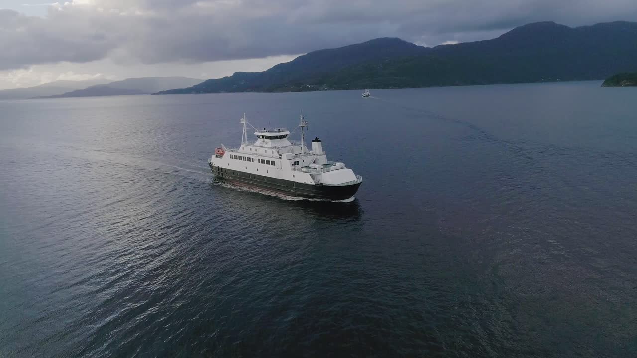 slomo aéreo volando hacia un ferry noruego durante la puesta de sol con montañas en el fondo y un buen reflejo de agua