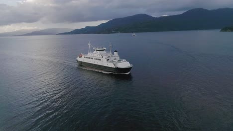 Luft-Slomo,-Der-Bei-Sonnenuntergang-Auf-Eine-Norwegische-Fähre-Zufliegt,-Mit-Bergen-Im-Hintergrund-Und-Schöner-Wasserspiegelung