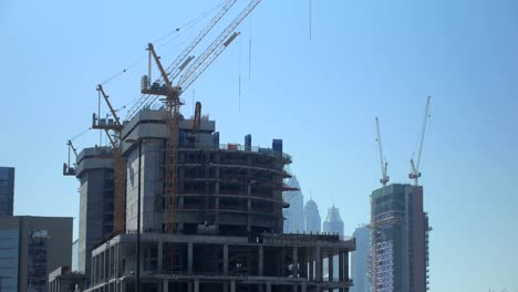 enormes grúas de construcción están en un edificio inacabado en una gran ciudad moderna, en un día de verano