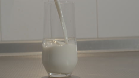 Milk-being-poured-into-glass-standing-on-kitchen-counter