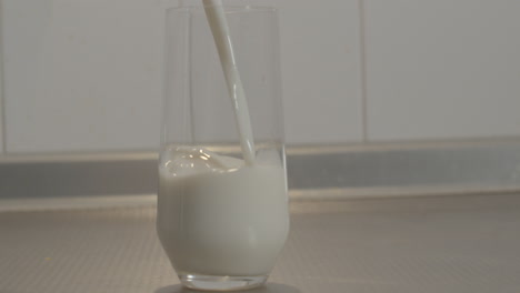 milk being poured into glass standing on kitchen counter