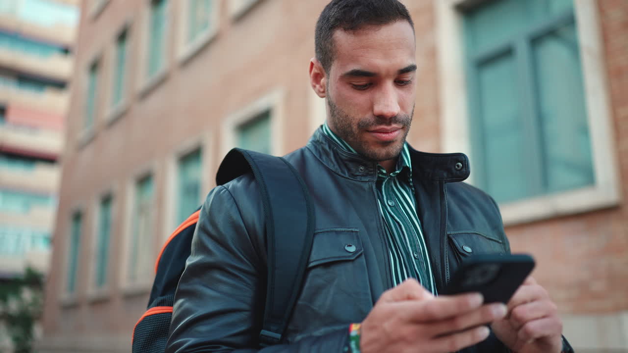 un joven enviando mensajes de texto en su teléfono inteligente al aire libre.