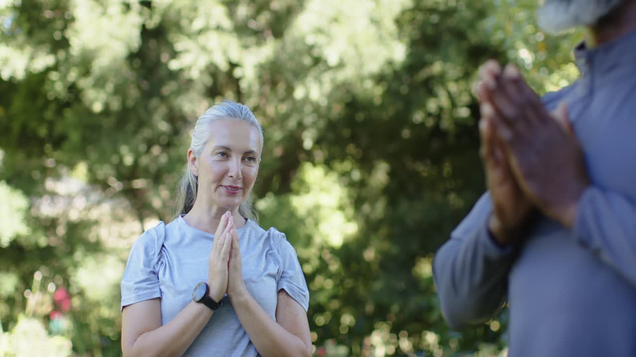 Diverses Paar meditiert im Park, Mann kommt herein und hält einen Gegenstand, Frau öffnet lächelnd mit Uhr die Augen