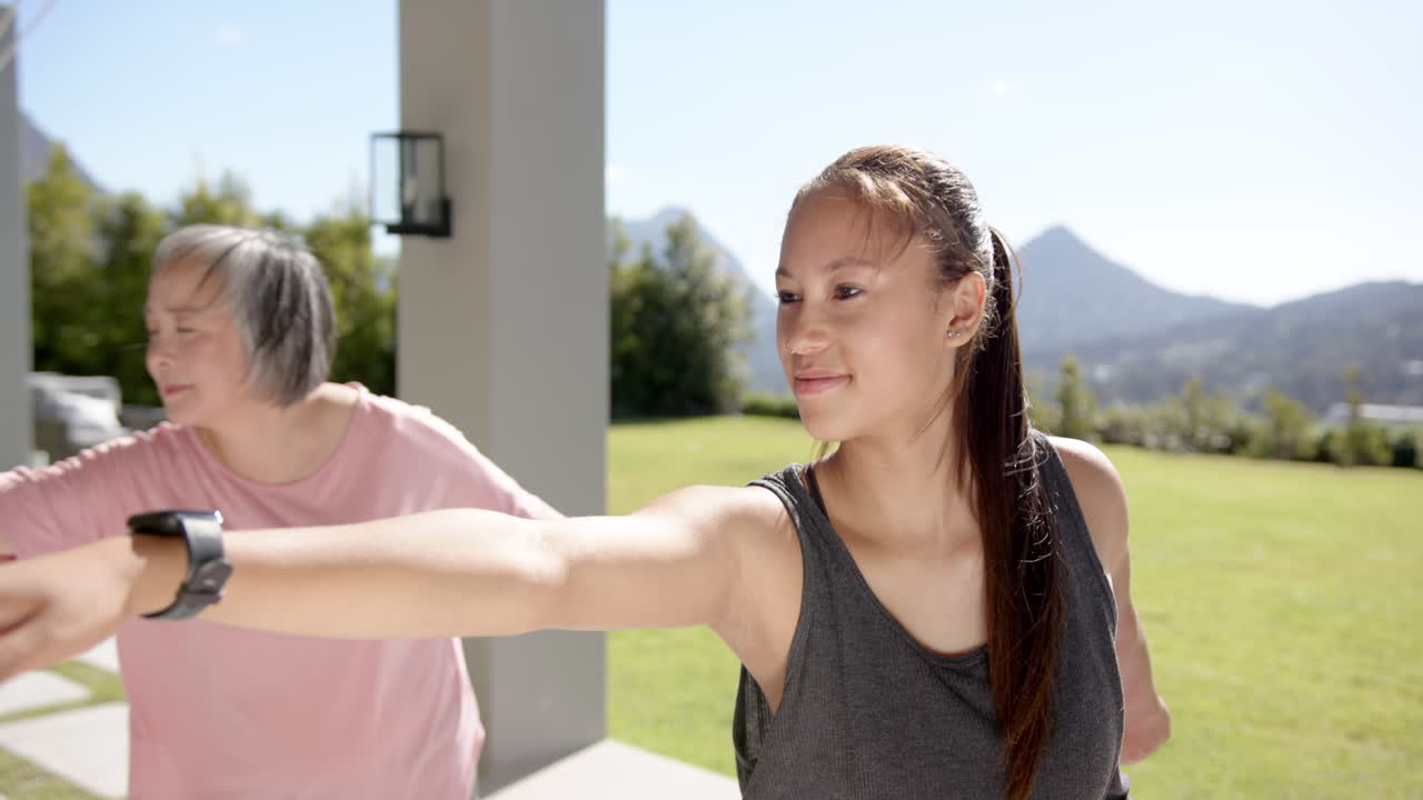 Exercising outdoors, young woman and older woman stretching arms together