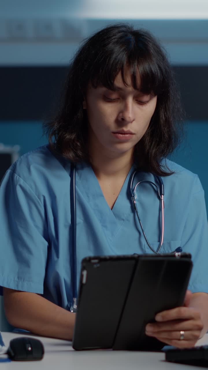 Vertical video: Medical nurse in blue uniform holding tablet computer analyzing patient expertise