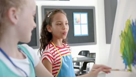 girls of diverse backgrounds paint on canvas in a classroom