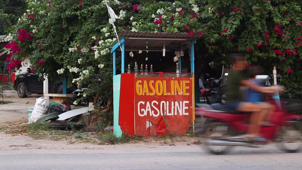 Motorbikes driving past vintage gasoline stand with glass bottles on Koh Phangan, Thailand.