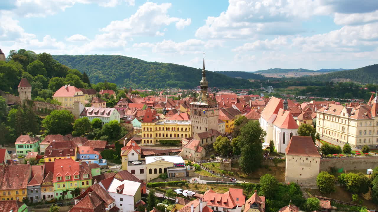 Lotniczy film poklatkowy z drona przedstawiający zabytkowe centrum Sighisoary w Rumunii. Stare budynki, wąskie uliczki z ludźmi, wieża zegarowa w Sighisoarze