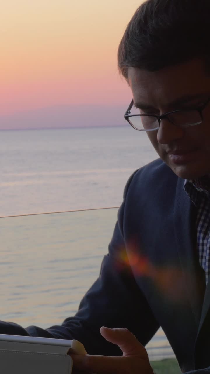 Uomo che fuma una sigaretta su un balcone con vista mare al tramonto