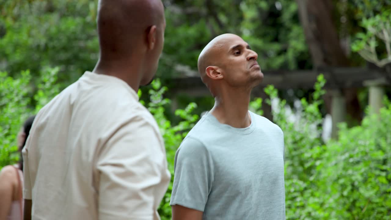 Diverse male friends standing in park prompted by friend's timing gesture, one checking watch