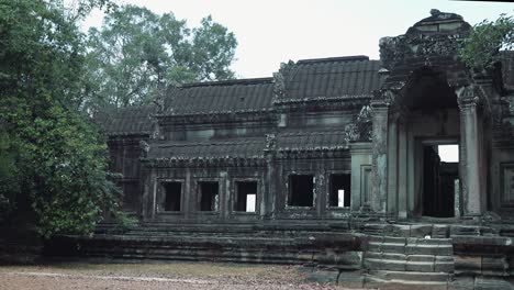 close exterior slow pan of grey ancient stone entrance to temple with windows and stairs surrounded by trees on a overcast cloudy day