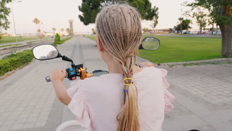 a child with african pigtails riding a scooter rear view cheerful and active recreation