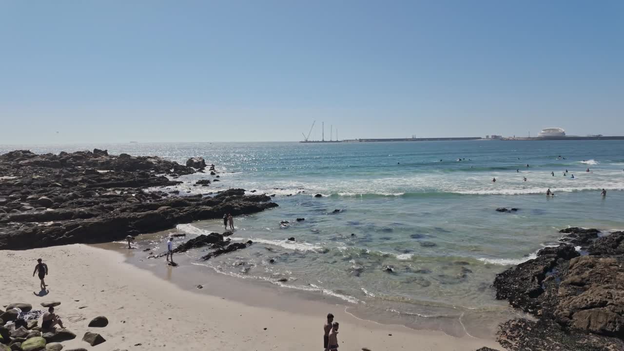 People enjoy a sunny day at Matosinhos Beach in Porto with buildings in the background