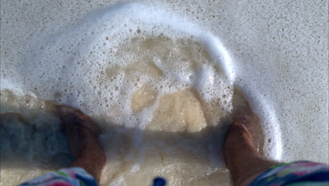 Slow-motion-POV-of-a-latin-man-standing-on-the-sand-at-a-caribbean-beach-getting-wet-by-the-waves-Cancun-Mexico