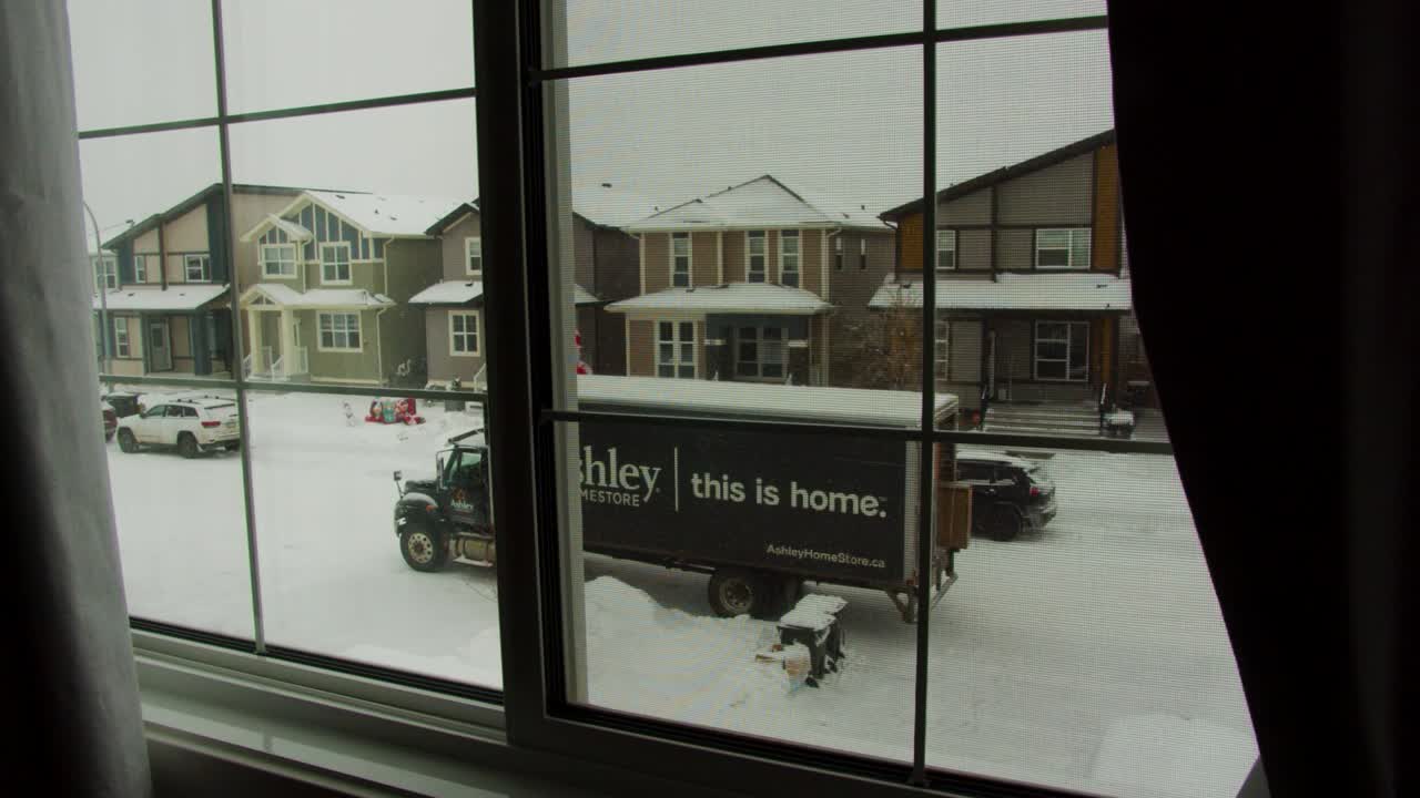 Shot looking outside through window at delivery truck parked on street in snowy suburban Canadian neighborhood
