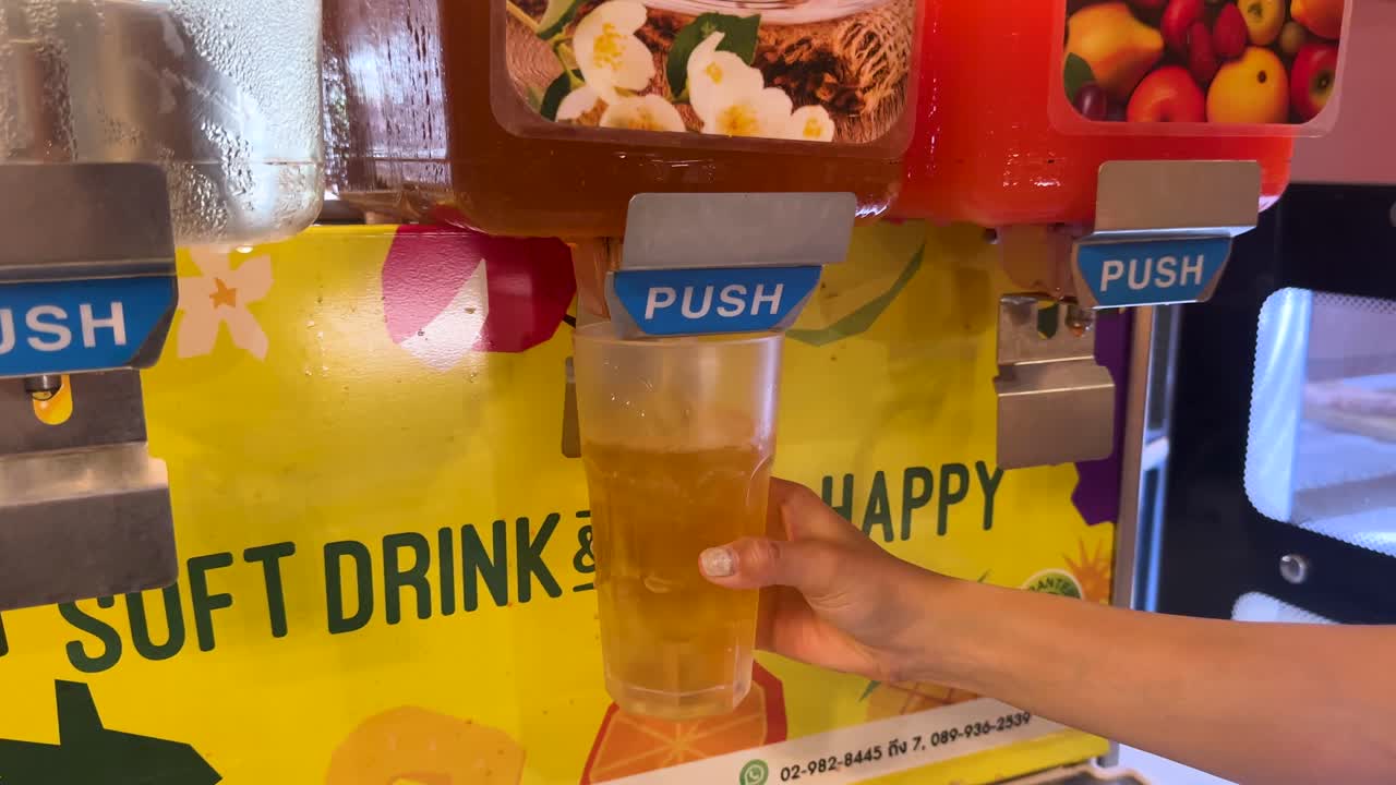 A hand fills a cup from a soft drink dispenser at a Korean BBQ in Bangkok. Bright, colorful setting