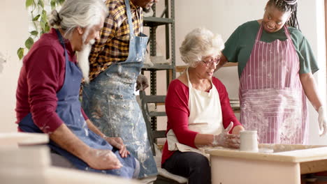 Happy-biracial-female-potter-with-others,-using-potter's-wheel-in-pottery-studio,-slow-motion