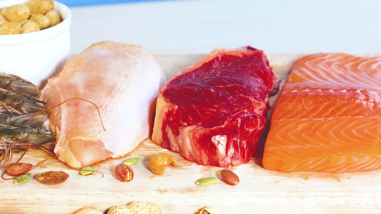 A vibrant display of various protein foods including meats, fish, and nuts, arranged on a wooden surface with bright lighting
