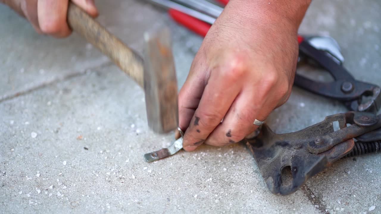 Dirty Caucasian male mechanic hands hammer steal clip on cement ground, close up static slow motion