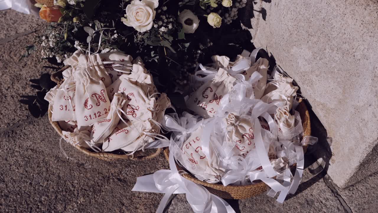 Nærbilde av bryllupsgaveposer med bånd i flettede kurver, omgitt av blomster