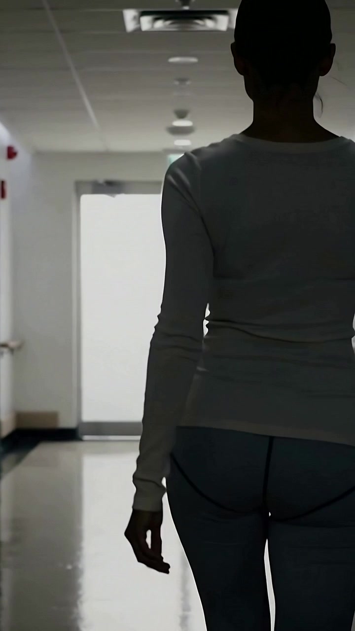 Video verticale: Donna che cammina con top chiaro e pantaloni scuri lungo un corridoio verso un'uscita, attratta da un bagliore luminoso.