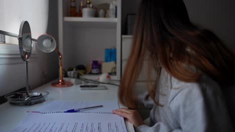 side close up of young girl studying on desk in dark, turns on lamp close to her