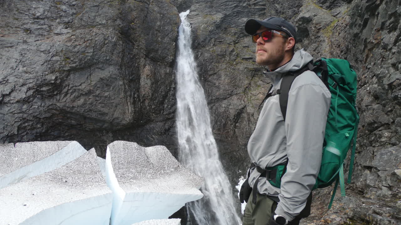 excursionista masculino con gafas de sol mirando la famosa cascada, silverfallet, norte de suecia