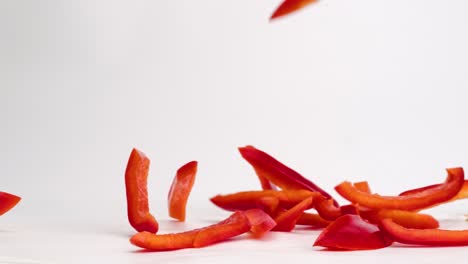 trozos de verduras de pimiento rojo cortado en juliana que caen sobre una mesa blanca en un montón a cámara lenta