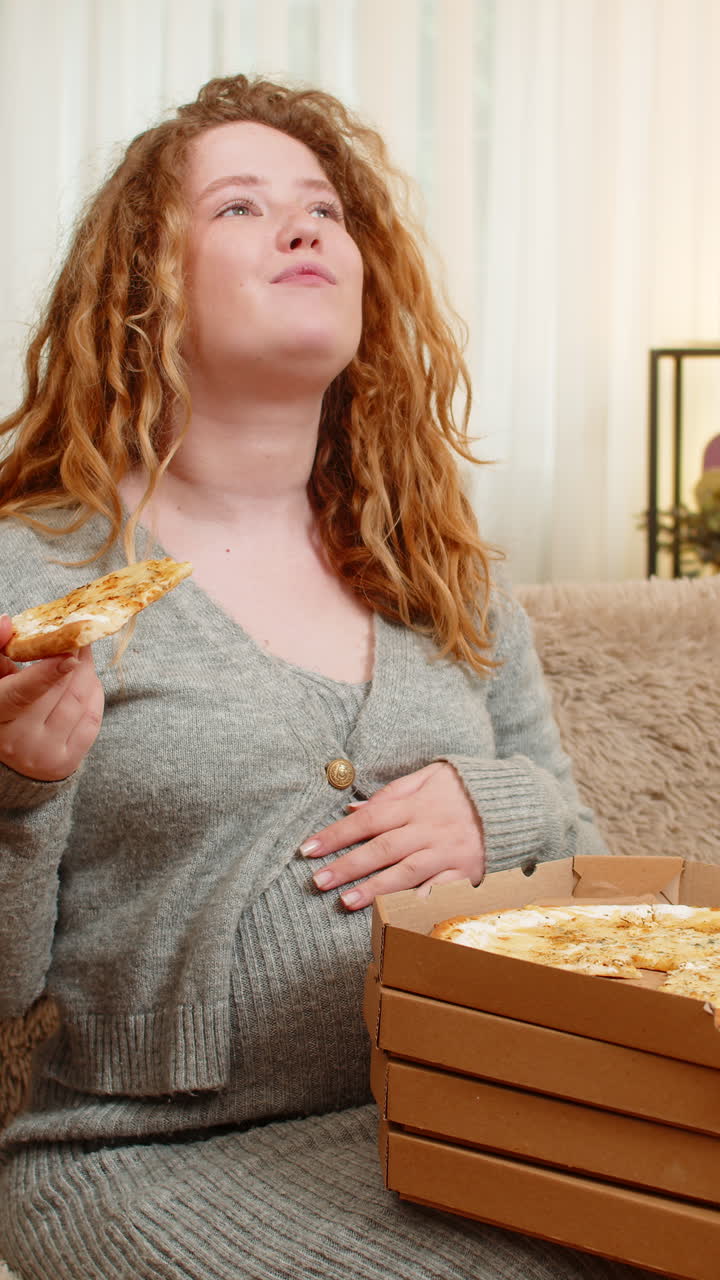Pregnant woman opening pizza box at home tasting slice with satisfied smile enjoying comfort food