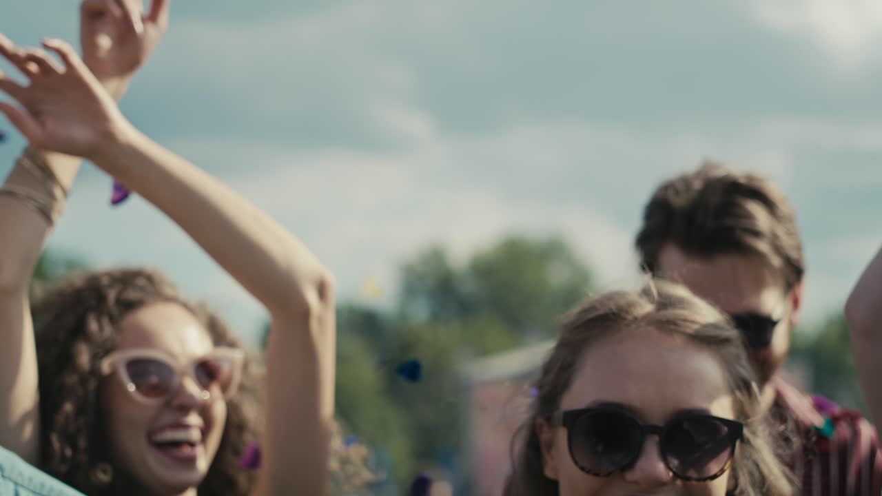 jóvenes amigos caucásicos bailando entre confeti en un festival de música con las manos en alto.
