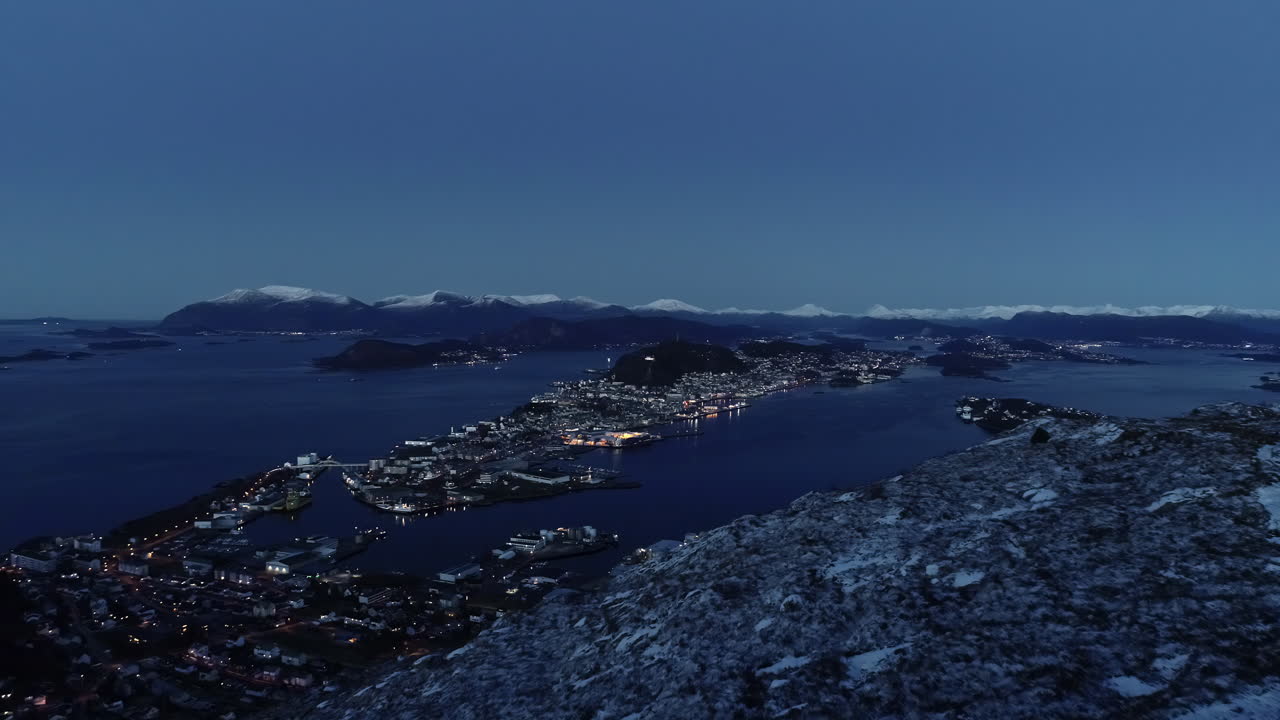 ночной снимок города в море с множеством огней рядом с горой зимой с высоты