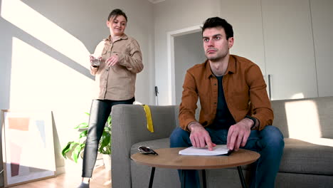 blind man reading a braille book sitting on sofa at home while his girlfriend bringing him a glass of water