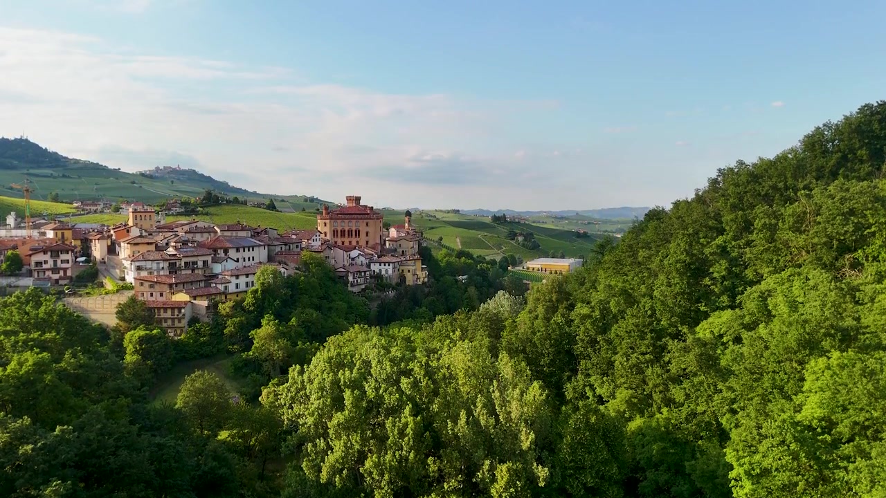 Ampia ripresa con drone rivela un villaggio e un castello storico italiano adagiato tra lussureggianti colline verdi.