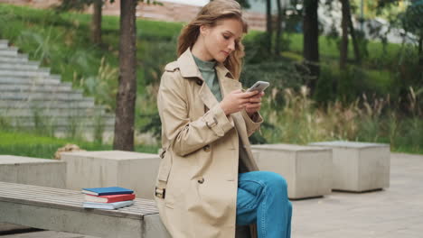 caucasian female student using smartphone outdoors.