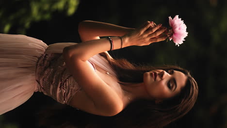 VERTICAL-Enchanting-long-haired-brunette-female-lovingly-holding-tropical-pink-flower-looking-at-camera-with-sensuality