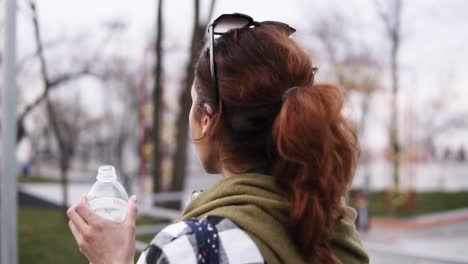 a girl with a tail walks on an overcast day in the park, drinks water from a plastic bottle. backside view. blurred background