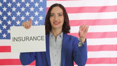 woman holding an "insurance" sign and a house key in front of an american flag