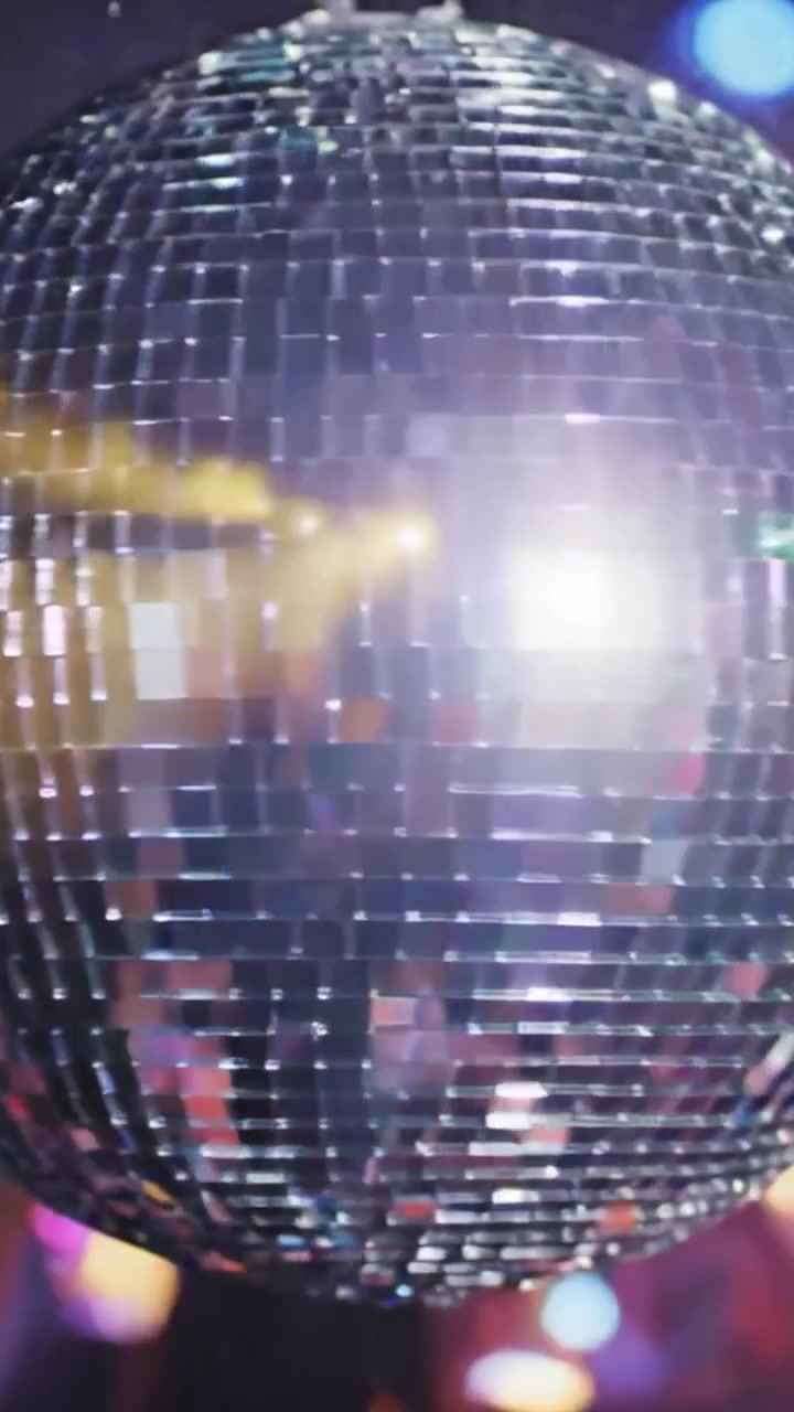 Un primo piano accattivante di una scintillante palla da discoteca con tessere riflettenti, che proietta motivi colorati in un'atmosfera vibrante piena di luci danzanti.