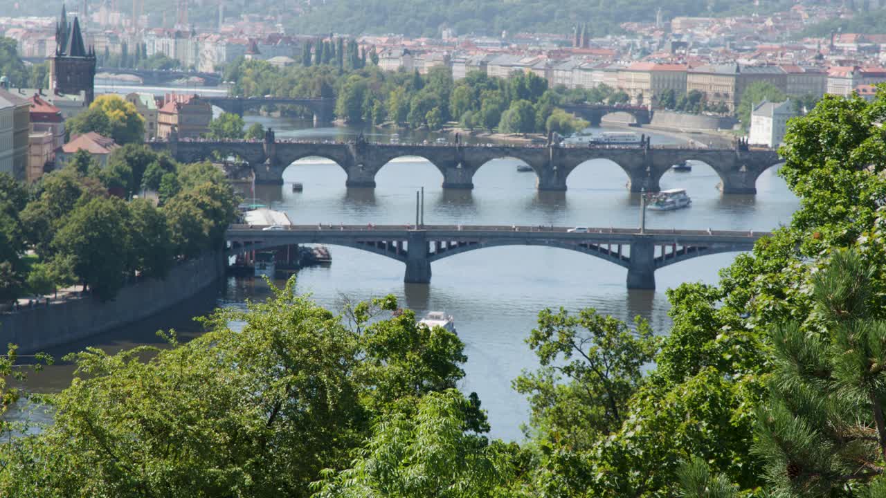 Wide aerial shot of Prague’s Vltava River bridges, cityscape, and greenery in bright daylight