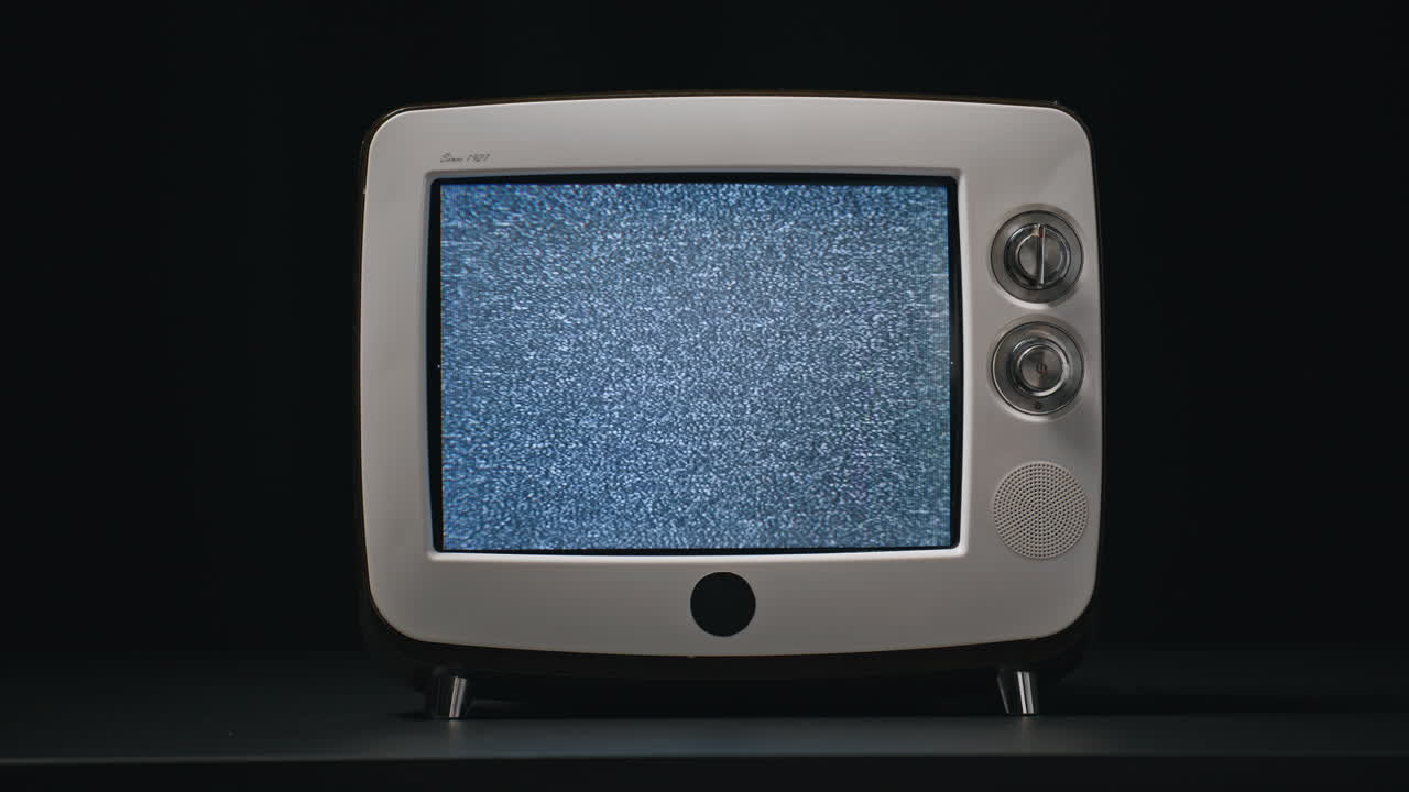 Primo piano di un vecchio schermo TV tremolante su un tavolo con sfondo nero. Rumore bianco