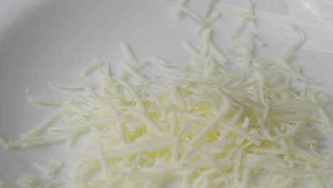 grated cheese falling onto a white plate.