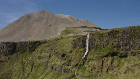 pintoresca cascada de islandia en un acantilado con una montaña volcánica en el fondo